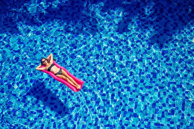 Mooie brunette meisje drijvend op matrassen in de pool.fitness vrouwelijk model in zwarte bikini rusten bij hotel swimmingpool.diet, sport en bodybuilding concept wateraerobics.