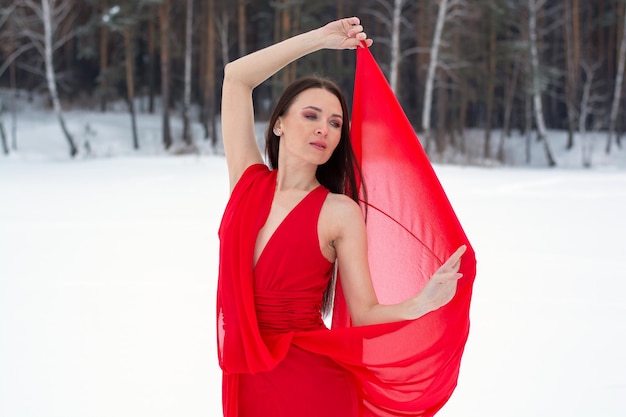 Mooie brunette meisje in een dunne rode jurk en blootsvoets in het winterbos