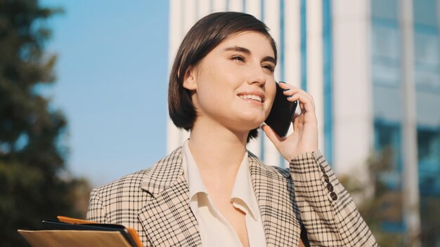 Mooie brunette meisje praten over smartphone wachten zakelijke bijeenkomst in het centrum. Zakenvrouw op straat in de stad