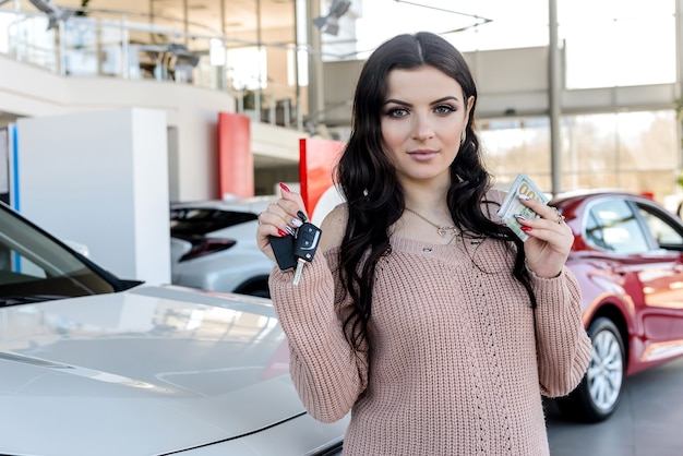 Mooie brunette met autosleutels en dollars in showroom