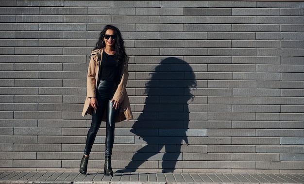 Mooie brunette met krullend haar en in zwarte kleren buiten in de buurt van de muur