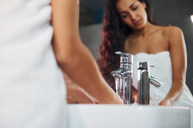 Mooie brunette staande in de badkamer in de buurt van de spiegel en handen wassen.