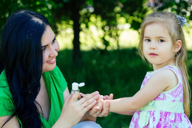 Mooie brunette vrouw alleenstaande moeder brengt antiseptische antibacteriële gel aan op de hand van dochterkind in het zomerpark