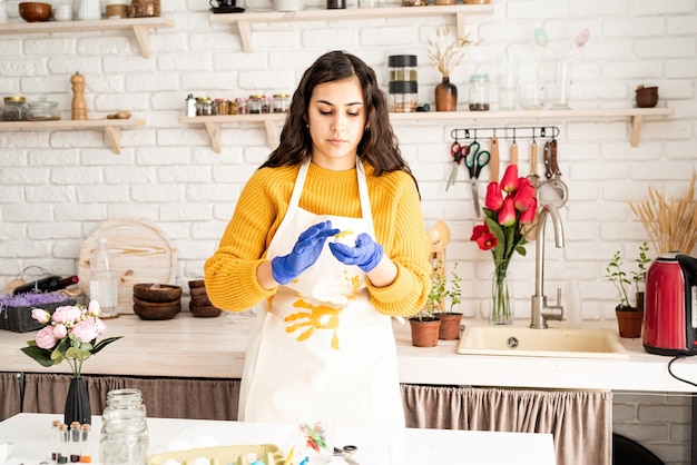Mooie brunette vrouw in gele trui en witte schort paaseieren in de keuken kleuren