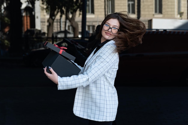 Mooie brunette vrouw met cadeau in haar handen op zwarte achtergrond. Gelukkig stijlvolle vrouw met zwarte doos in handen.