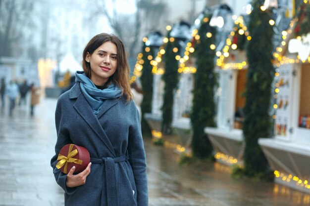 Mooie brunette vrouw met geschenkdoos in de buurt van de kerstmarkt. Ruimte voor tekst