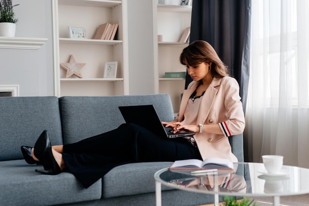 Mooie brunette vrouw ontspannen met haar laptop terwijl ze op een bank in de woonkamer ligt