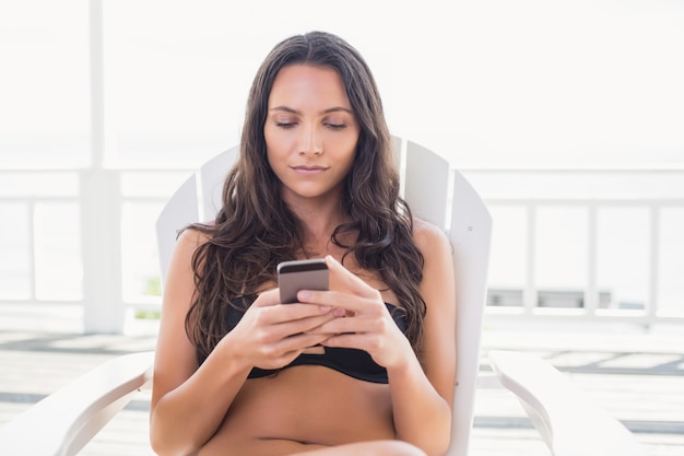 Mooie brunette zittend op een stoel en sms met haar mobiele telefoon