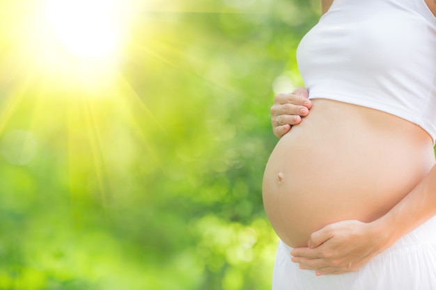 Mooie buik van jonge zwangere vrouw tegen groene lente achtergrond