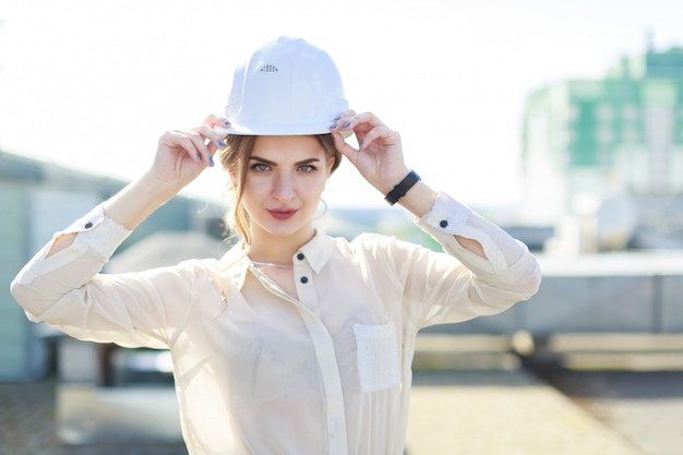 Mooie businesslady in witte blouse, horloge, helm en zwarte rok staan op het dak