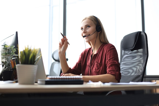 Mooie callcentermedewerker in koptelefoon werkt op modern kantoor.