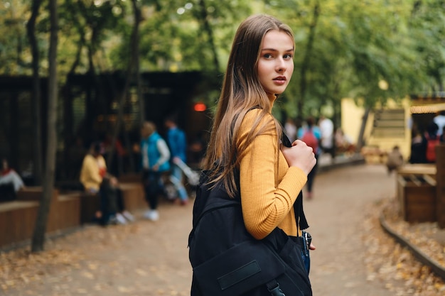 Mooie casual student meisje met rugzak aandachtig in de camera kijken in stadspark
