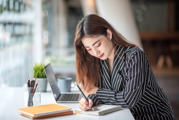 Mooie, charmante Aziatische bedrijfsvrouw die met een laptop computer aan een modern bureau werkt