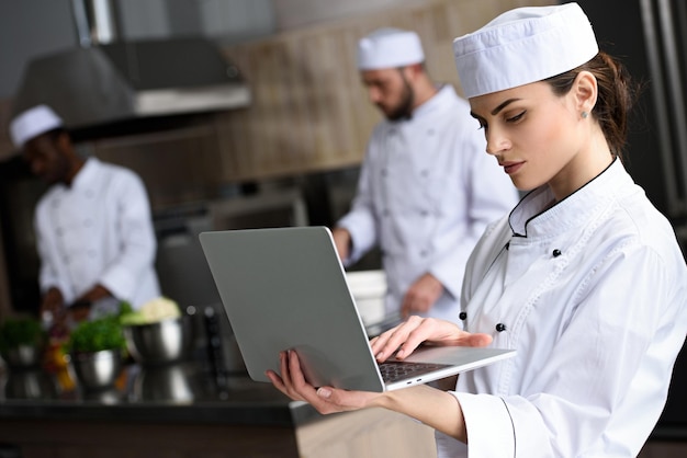 Mooie chef-kok die laptop met behulp van bij restaurantkeuken