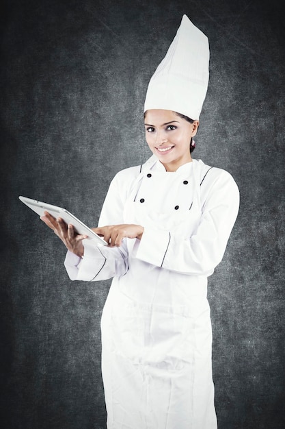 Mooie chef-kok met behulp van een tablet in de studio