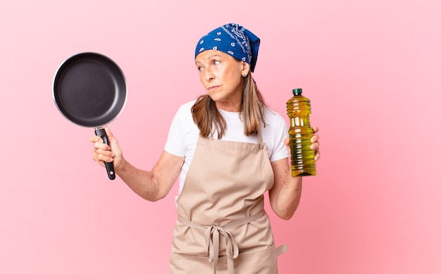 Mooie chef-kokvrouw van middelbare leeftijd die een pan en een olijfoliefles houdt