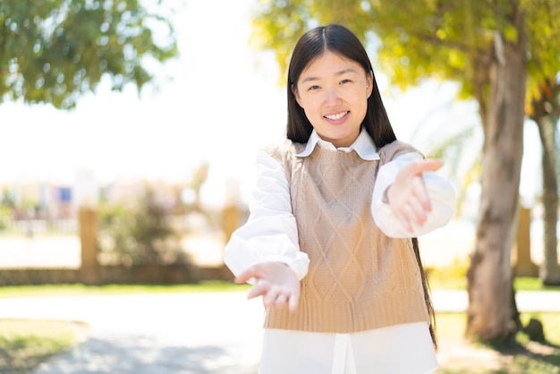 Mooie chinese vrouw die buiten presenteert en uitnodigt om met de hand te komen