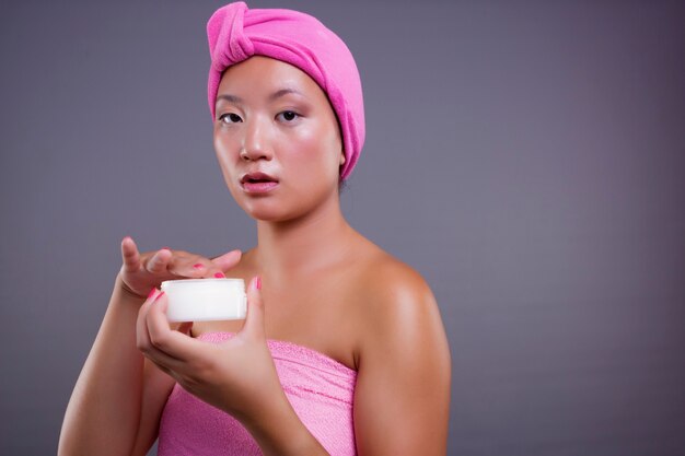 Mooie Chinese vrouw die voor haar huid zorgt, geïsoleerd van het grijze achtergrondschoonheidsconcept