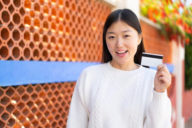 Mooie Chinese vrouw met een creditcard buitenshuis met verrassing en geschokte gezichtsuitdrukking