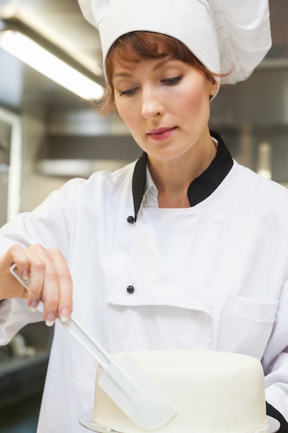 Mooie concentrerende chef-kok die een cake met suikerglazuur beëindigt