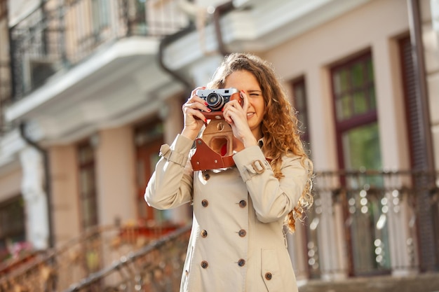 Mooie curlyhaired blanke vrouw met een retro camera in het concept van het stadstoerisme