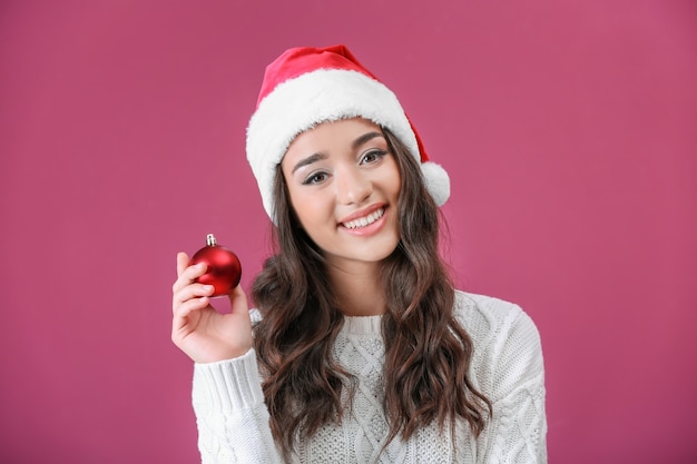 Mooie dame in kerstmuts met glanzende snuisterij op kleur achtergrond