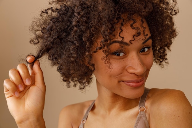 Mooie dame met krullend kapsel poseren tegen beige muur