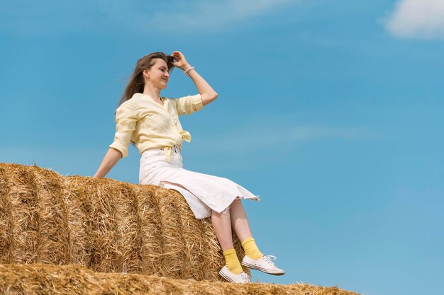 Mooie dame zit op stro en poseert voor foto weekend op het platteland zomerdag blauwe hemelachtergrond