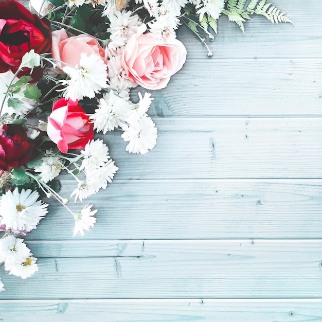 Mooie decoratieve compositie van bloemen op een blauwe houten tafel. Plat lag, bovenaanzicht, close-up, vierkante achtergrond met kopieerruimte voor uw tekst. Rode en roze rozen, margrieten, greens.