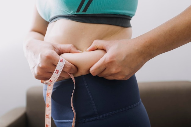 Mooie dikke vrouw met meetlint Ze gebruikt haar hand om het overtollige vet te persen dat op een witte achtergrond is geïsoleerd. Ze wil afvallen, het concept van chirurgie en vet afbreken onder de