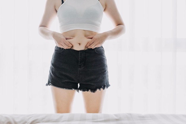 Mooie dikke vrouw met meetlint Ze gebruikt haar hand om het overtollige vet te persen dat op een witte achtergrond is geïsoleerd. Ze wil afvallen, het concept van chirurgie en vet afbreken onder de