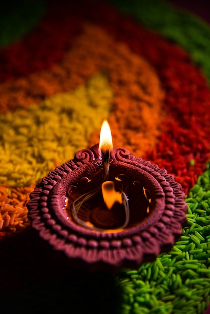 Mooie Diwali-begroeting met behulp van Diya of klei-olielamp verlicht en gerangschikt over Rangoli gemaakt door meerkleurige rijstkorrels, selectieve focus