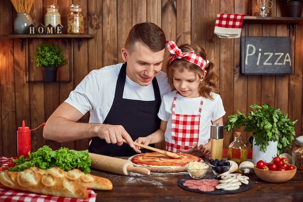 Mooie dochter die papa helpt om saus uit te spreiden terwijl het koken van pizza