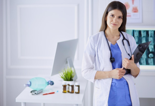 Mooie dokter staat in een spreekkamer met een map in haar handen, denkend