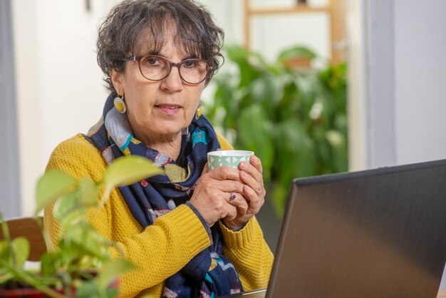 Mooie donkerbruine rijpe vrouw die in gele het drinken kop thee draagt