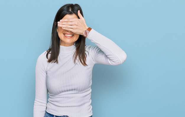 Mooie donkerbruine vrouw die casual kleding draagt die glimlacht en lacht met de hand op het gezicht die de ogen bedekt voor verrassing blind concept