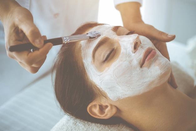 Mooie donkerbruine vrouw die geniet van het aanbrengen van een cosmetisch masker met gesloten ogen. Ontspannende behandeling in geneeskunde en spa-concepten