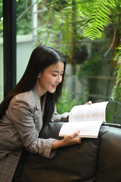 Mooie duizendjarige vrouw die een boek leest terwijl ze op de bank op haar kantoor rust