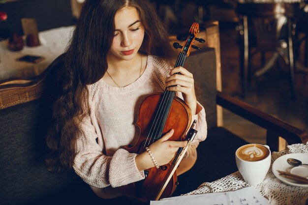 mooie elegante meisjeszitting in een koffie met viool en het drinken van koffie