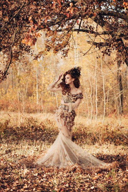 Mooie elegante vrouw die zich in de herfst bos in chiffon jurk met gele herfstbladeren