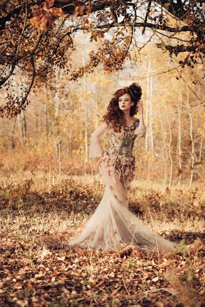Mooie elegante vrouw die zich in de herfst bos in chiffon jurk met gele herfstbladeren