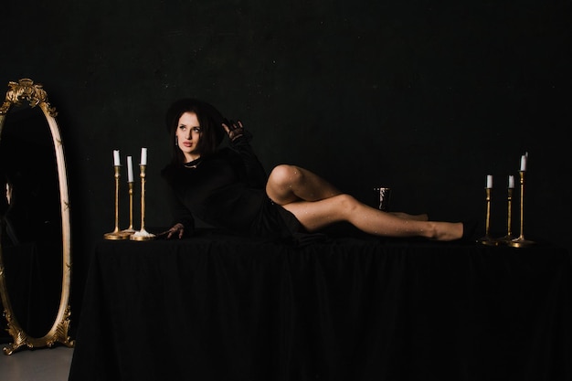 Mooie elegante vrouw in handschoenen en een jurk zit op een tafel op een zwarte achtergrond