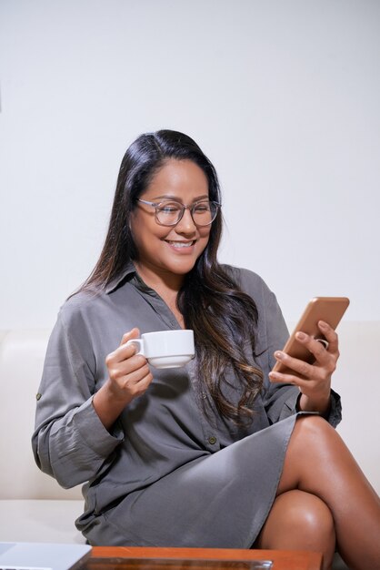 Mooie elegante zakenvrouw die koffie drinkt en berichten op sociale media beantwoordt of meldingen op smartphone controleert