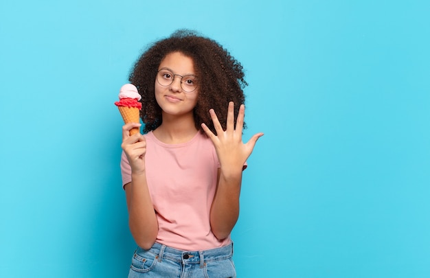 Mooie en afro-tiener die vriendelijk glimlacht kijkt, nummer vijf of vijfde met vooruit hand toont, aftellend