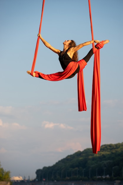 Mooie en flexibele vrouwelijke circusartiest die danst met luchtzijde op een hemelachtergrond.