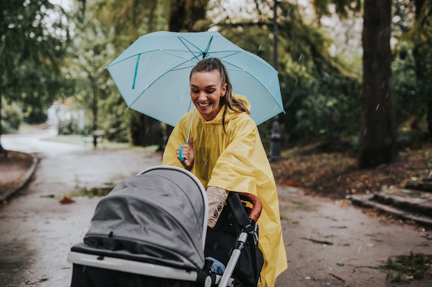 Mooie en gelukkige vrouw van middelbare leeftijd met haar baby die op regenachtige dag in het stadspark loopt