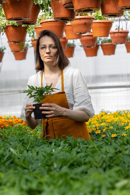 Mooie en jonge volwassen blanke vrouw tuinman in een kas of plantenkwekerij zorgt voor