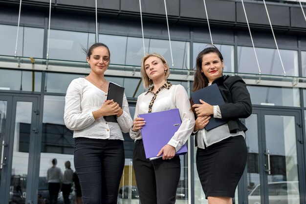 Mooie en jonge zakenvrouwen met documenten en mappen poseren buiten kantoorgebouw