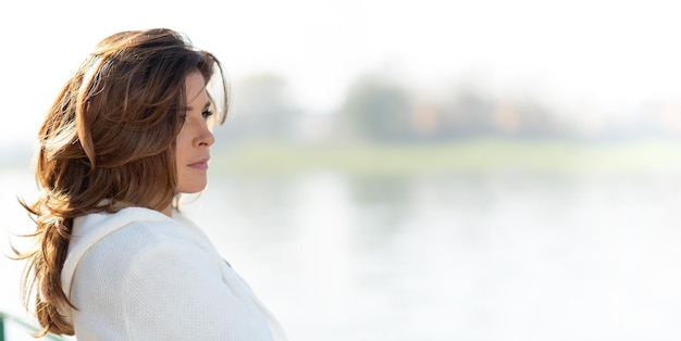 Foto mooie en sensuele vrouw kijkt bedachtzaam naar het idyllische landschap van de kust of rivier in de stad verlicht door diepe ochtendlicht kopieerruimte