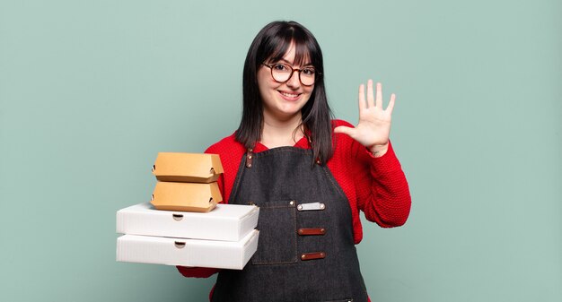 Mooie en vrouw die vriendelijk glimlacht kijkt, nummer vijf of vijfde met vooruit hand toont, aftellend